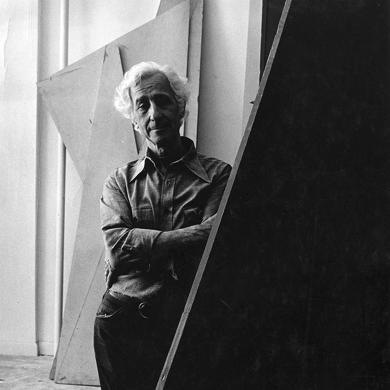 Black and White portrait of Tony Rosenthal crossing arms next to sculpture